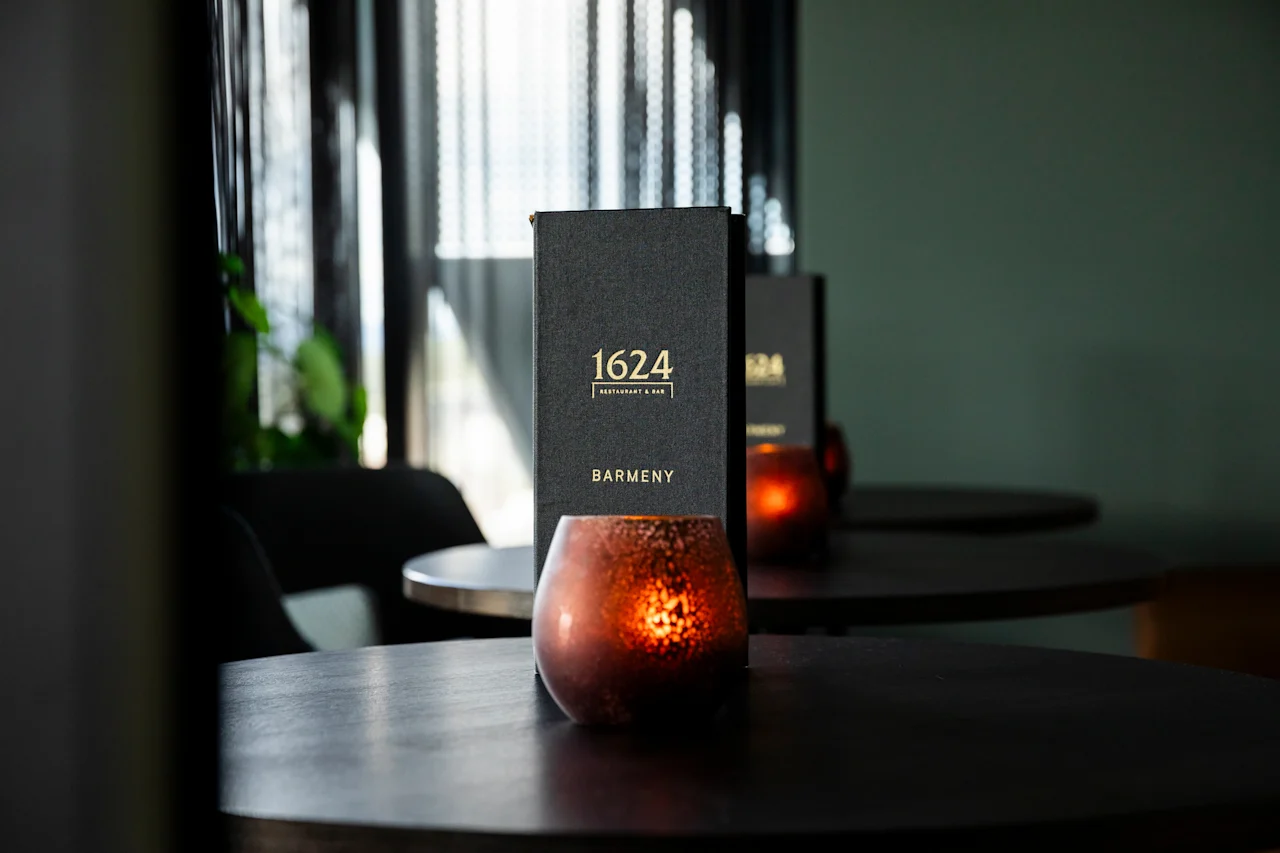En koselig barscene med en meny for "1624 Restaurant & Bar" og "Barmeny" på et mørkt bord ved siden av et glødende lys.