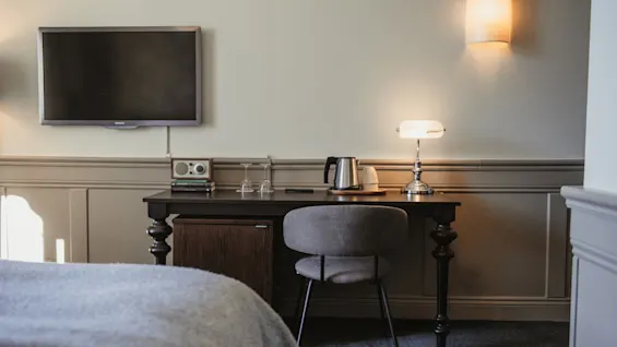 Ett hotellrums skrivbordsområde med en TV, en lampa och kaffefaciliteter, redo för gästanvändning.