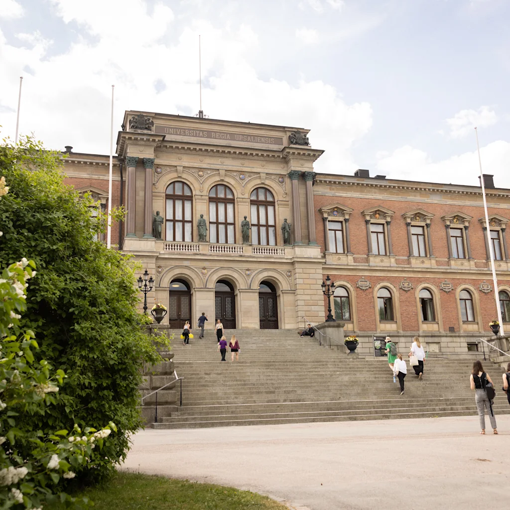 Suuri yliopistorakennus, jossa on suuret portaat ja ihmisiä kävelemässä. Teksti rakennuksessa: UNIVERSITAS REGIA UPSALIENSIS.