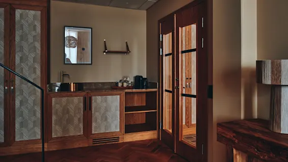 Et sofistikert rom med fiskebensparkett, et stilig forfriskningsområde og doble glassdører til et annet rom.