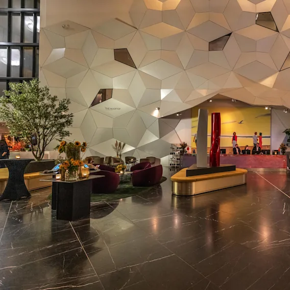 En geometrisk væg med sekskantede mønstre skaber overblik over en rummelig lobby med moderne møbler og kunstværker. Teksten på væggen lyder "THE ROOFTOP". Der er planter og siddeområder.