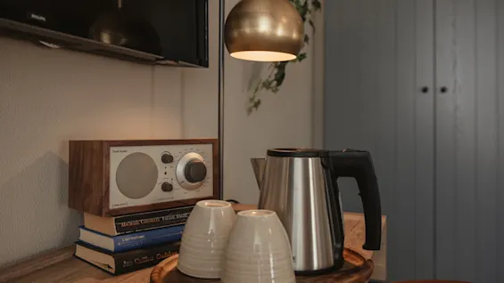 A cozy corner with a radio (MODEL ONE, AM/FM, AUX IN), books, kettle, and cups on a tray, for a relaxing break.