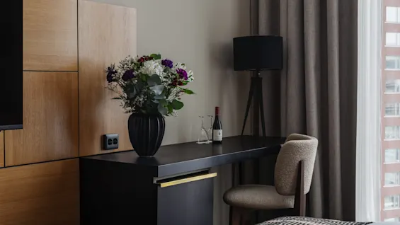 Et koselig hotellrom med skrivebord, stol og en vase med friske blomster, som antyder et komfortabelt opphold.