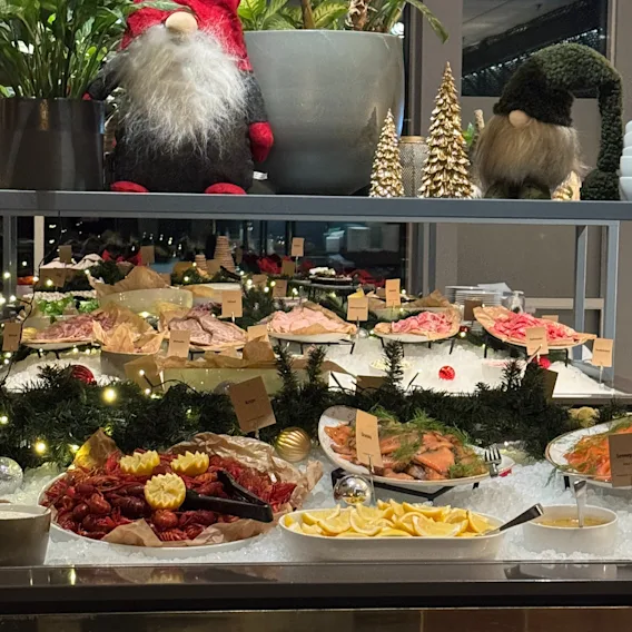En innbydende julebuffet med fersk sjømat og andre kalde retter, pyntet med festlige nisser og små dekorative trær.