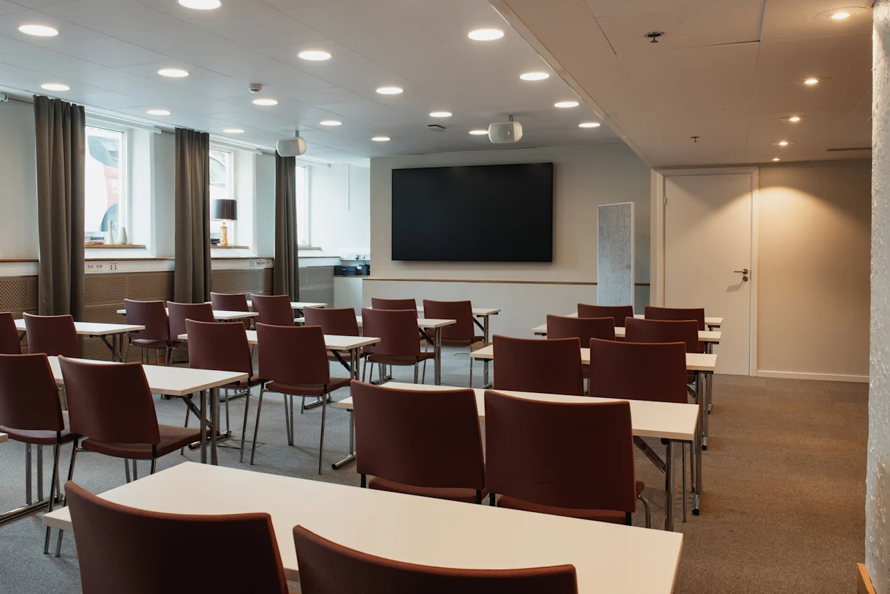 A modern conference room at Home Hotel Uppsala with rows of tables and chairs facing a large screen, ready for a presentation.