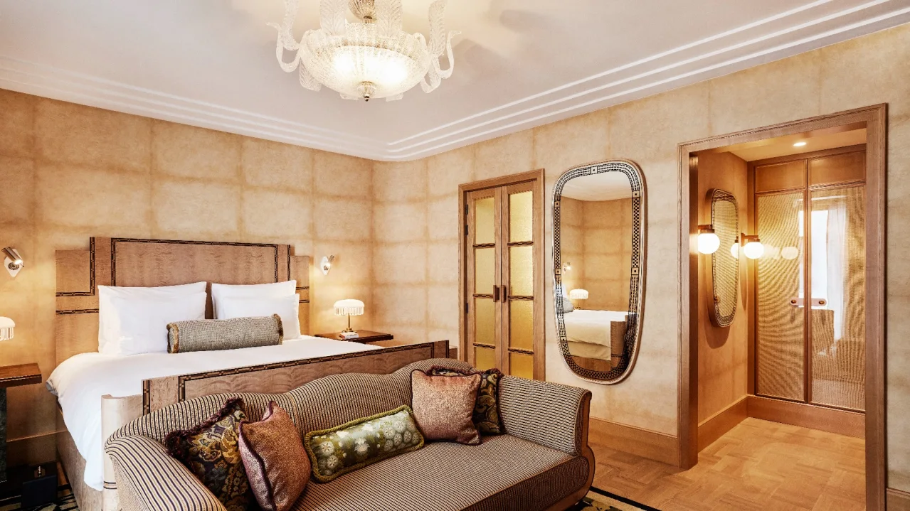 An elegant bedroom with a plush bed, sofa, chandelier, and a mirror reflecting another room.