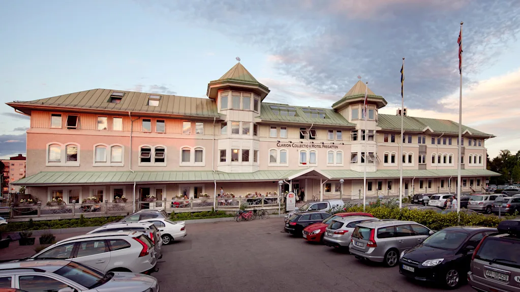 Ett historiskt hotell med en terrass och gäster vid skymning, omgivet av parkerade bilar.