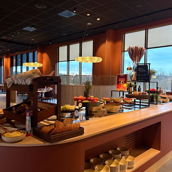 En deilig frokostbuffé med ferskt brød, bakverk og frukt, servert i et moderne spiseområde med store vinduer.