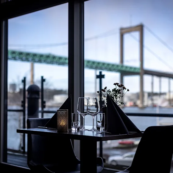 Ett dukat restaurangbord vid ett fönster med utsikt mot en stor bro över vattnet.