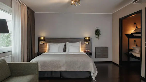 Viihtyisä hotellihuone, jossa on suuri sänky, mukava sohva ja erillinen kerrossänkyalue lisävieraille.