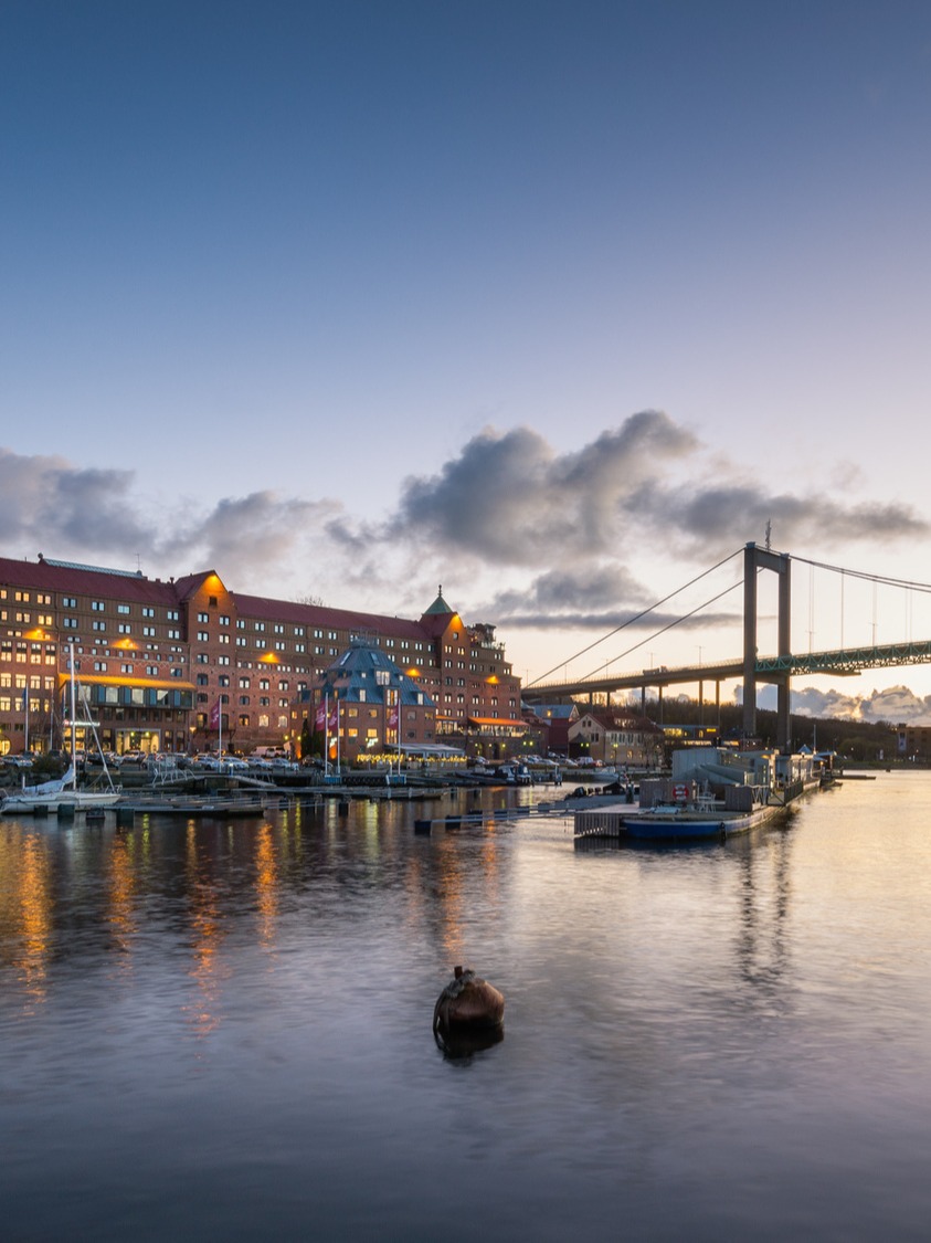 Quality Hotel Waterfront in Gothenburg at dusk, seen from the water with a bridge in the background.