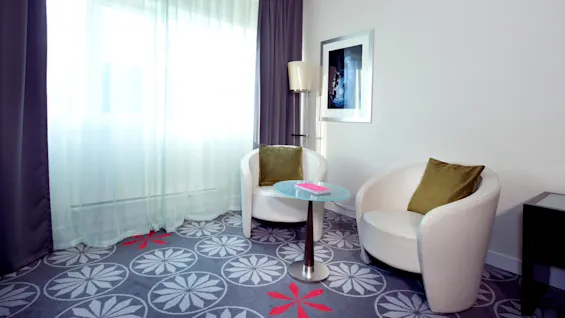 A well-lit room with two white chairs, a side table, a floor lamp, and a framed picture, suggesting a modern interior setting.