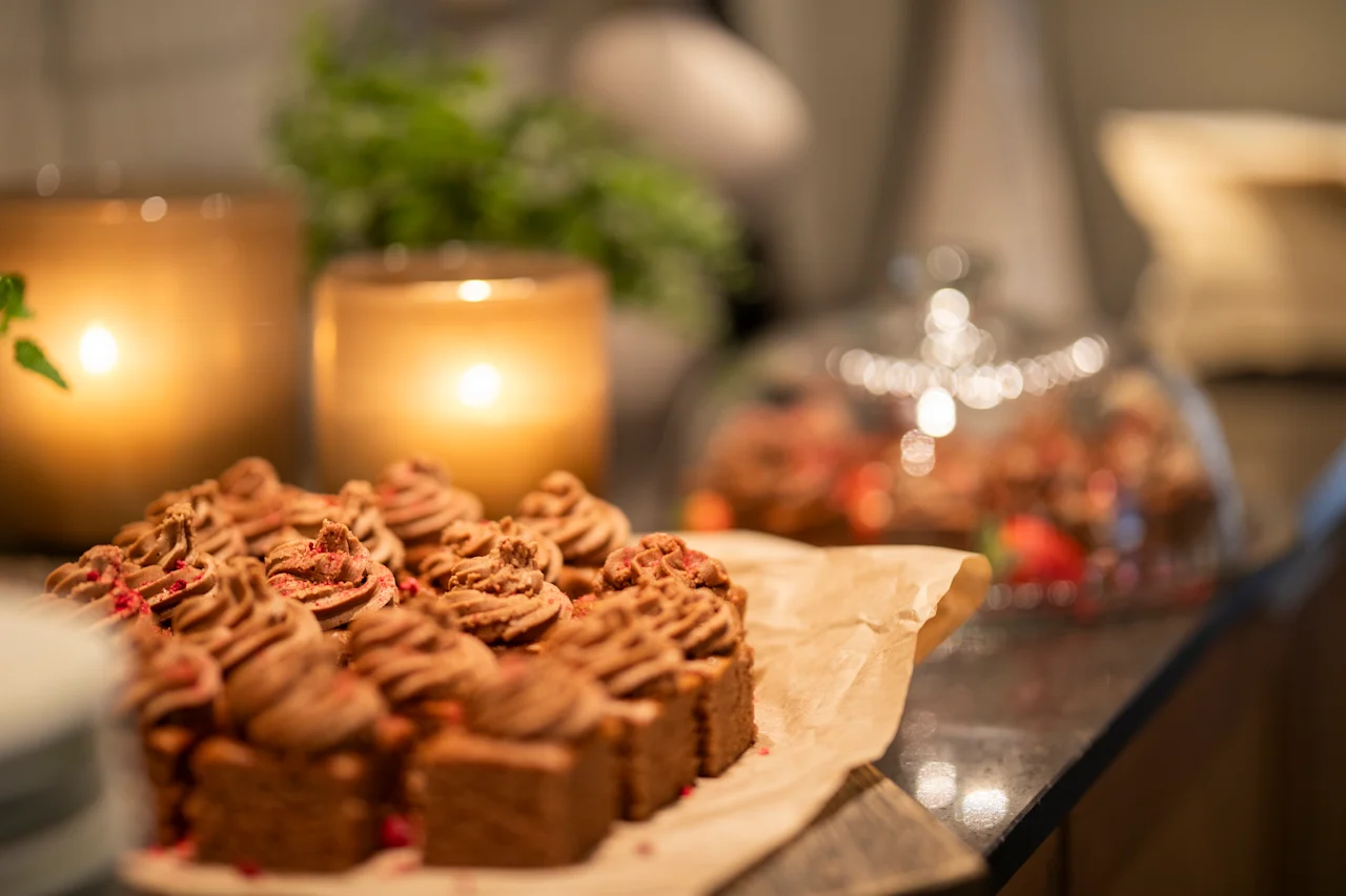 Sjokoladekaker er pent arrangert på bakepapir, omgitt av tente lys, en glassklokke og grønt på et trebord, som skaper en koselig, inviterende atmosfære.