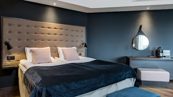 Moderni hotellihuone, jossa on suuri parivuode, tummansiniset seinät ja tyylikäs sängynpääty.