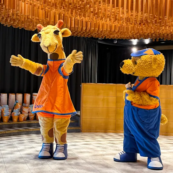 Lollo-kirahvi ja Bernie-karhu -maskotit seisomassa sisätilassa, jossa on näyttävä puukatto.