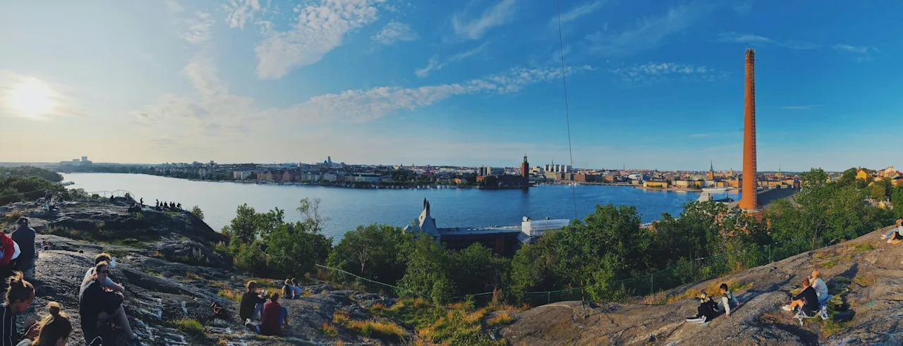 People relaxing on a rocky hill, enjoying the panoramic view over Stockholm with its city skyline and a large body of water.