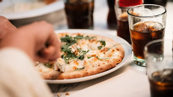 Enjoying a meal with pizza topped with cheese and greens, accompanied by refreshing drinks.