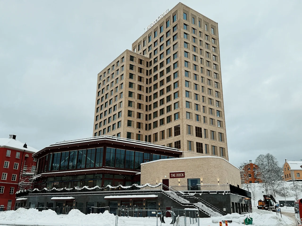 En moderne, høy bygning med en lavere del, med et skilt som leser THE DOCK, omgitt av snø en overskyet vinterdag.