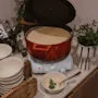 En röd gryta med krämig soppa värms på en platta, omgiven av staplade skålar och färsk persilja i en kruka på en disk.