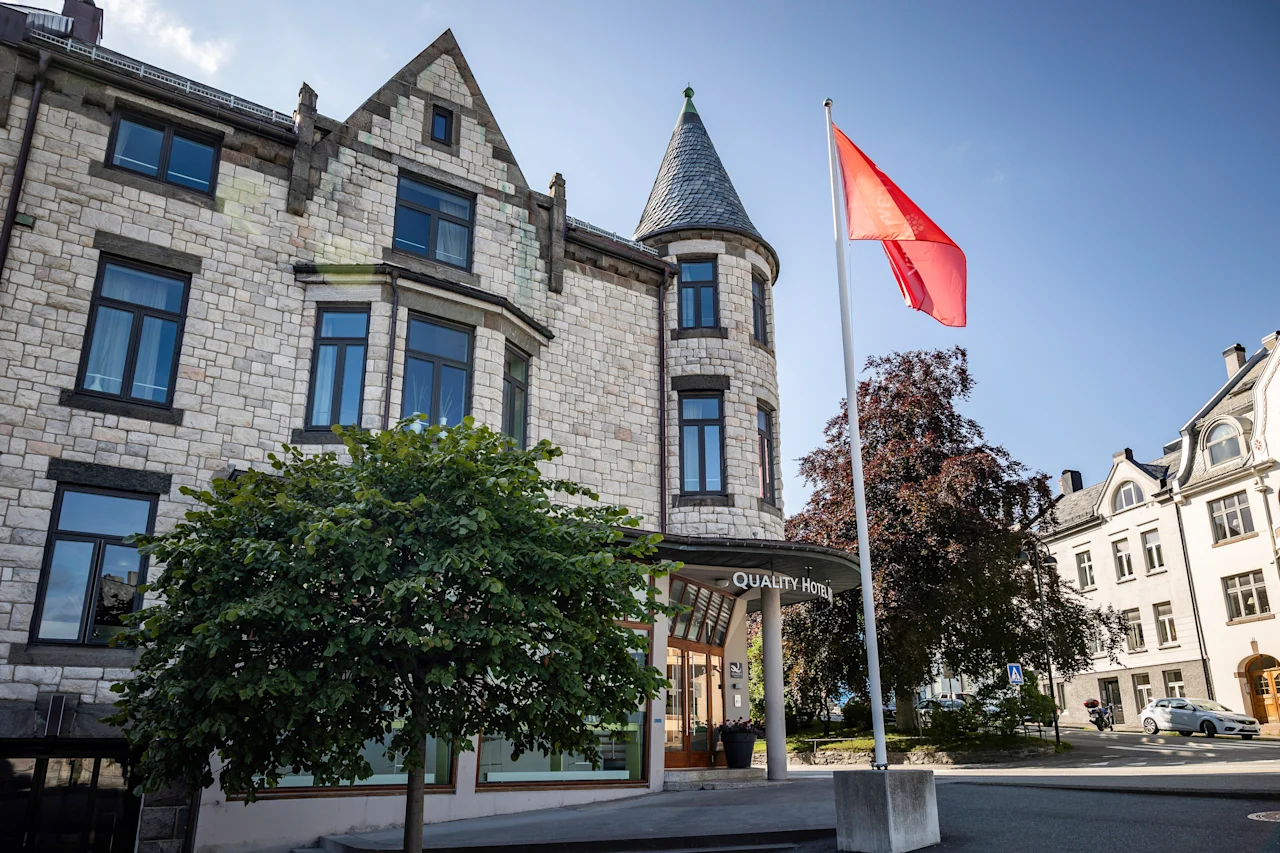 En steinbygning med et tårn og et rødt flagg som vaier. Inngangen har et skilt hvor det står "Hotell".