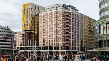 Människor går på en stadsgata framför en hög byggnad med texten CLARION THE HUB, omgiven av andra stadsstrukturer.