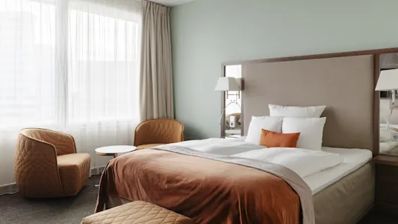 Ett mysigt hotellrum med en stor säng, två bekväma fåtöljer och mjuk belysning, perfekt för avkoppling.