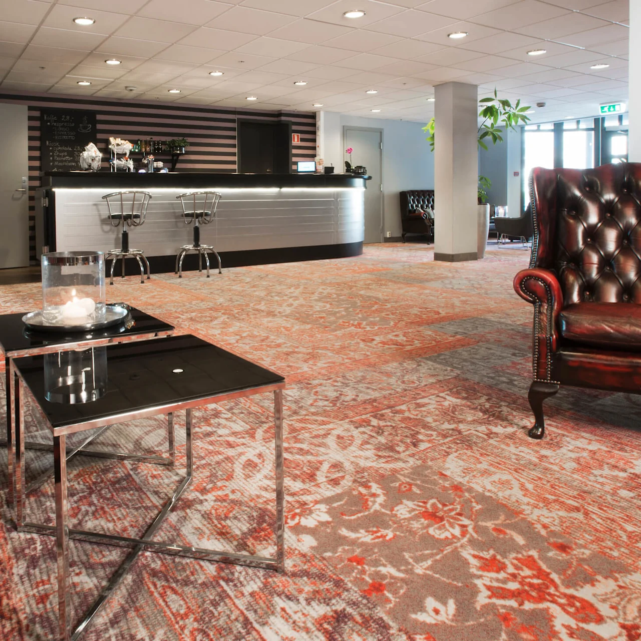 Lädersoffa och glasbord i en hotelllobby med bardisk och dekorativ matta.