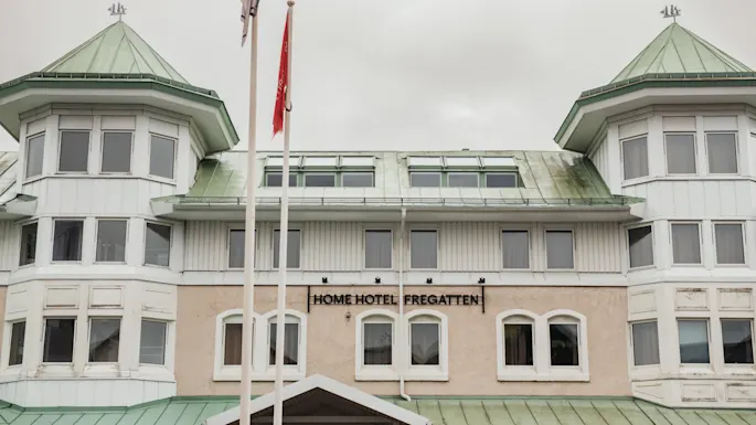 Utvendig utsikt over en hotellbygning med grønne tak og karnapper. Et skilt på fasaden leser HOME HOTEL FREGATTEN.
