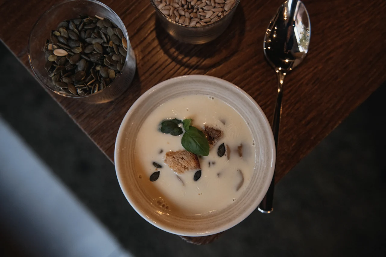 Herkullinen kermainen keitto, koristeltu krutongeilla, kurpitsansiemenillä ja tuoreella basilikanlehdellä, valmiina nautittavaksi.