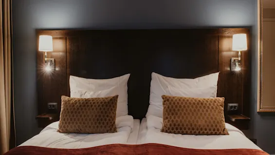 A comfortable bed in a hotel room with warm lighting, ready for a relaxing stay at Home Hotel Kung Oscar.