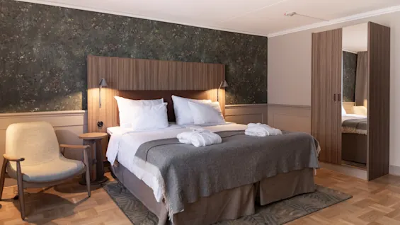 Home Hotel Tapto: Ett mysigt hotellrum med en stor säng, två badrockar och en bekväm fåtölj, redo för avkoppling.