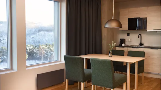 Et hyggeligt spiseområde og køkken med et stort vindue, der vender ud mod en sneklædt skov.