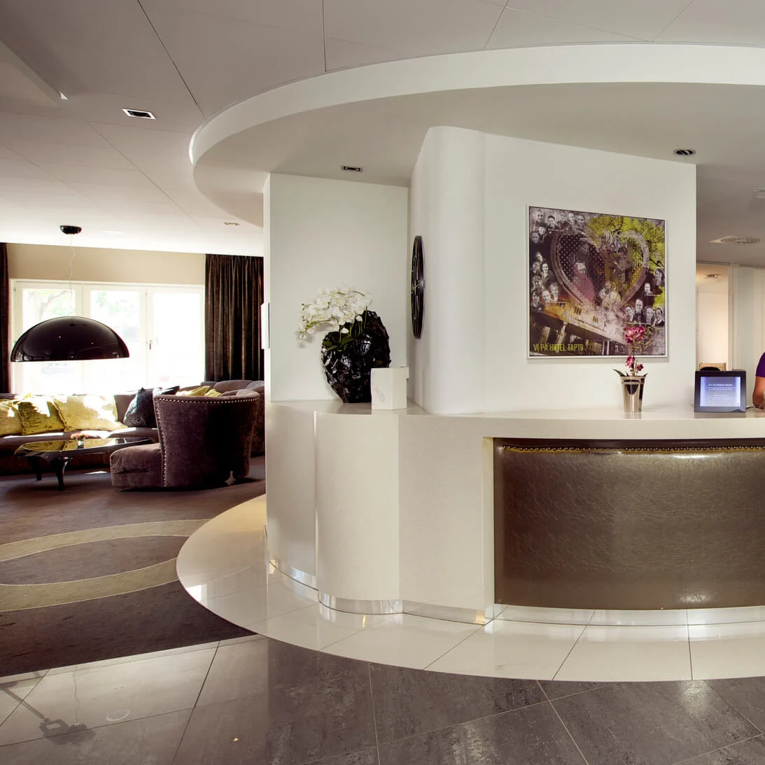 Two staff members work at a curved reception desk in a modern hotel lobby.