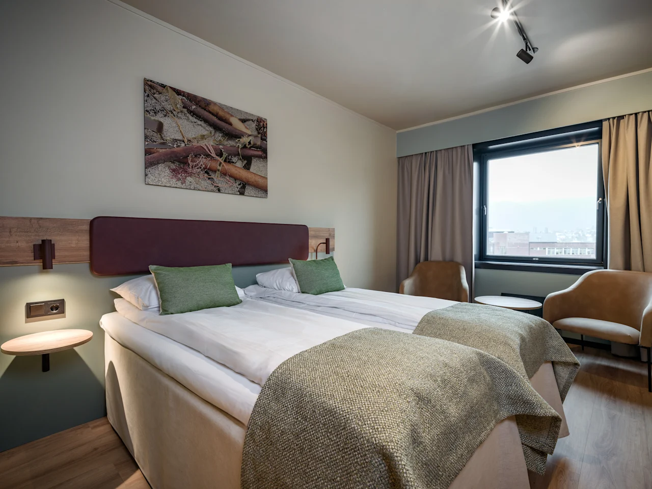 Mukava hotellihuone, jossa on kaksi sänkyä, suuri ikkuna ja kaksi nojatuolia, mikä viittaa rentouttavaan oleskeluun.