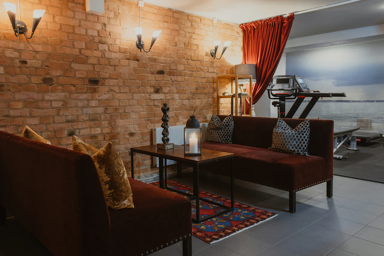 En mysig lounge med tegelväggar och soffor, intill ett gym med löpband och en naturskön väggmålning på Home Hotel Grand, Helsingborg.