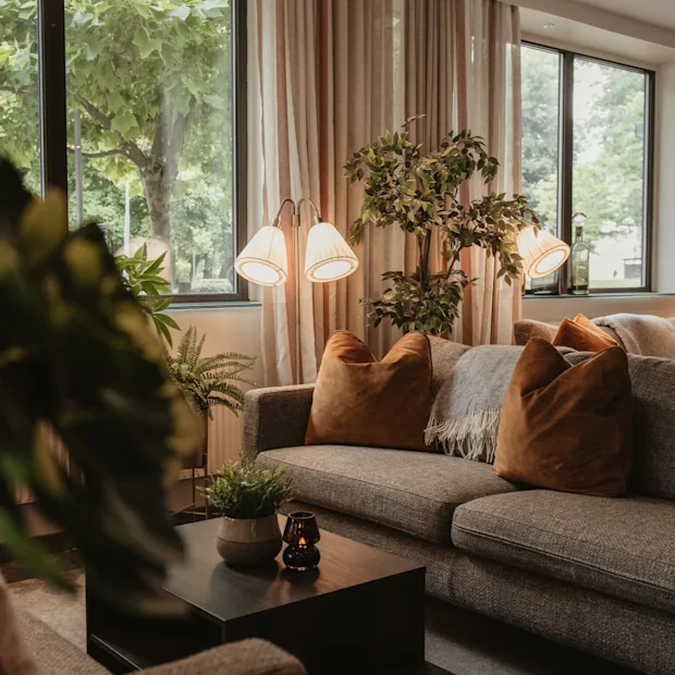 A cozy lounge area with comfortable sofas, warm lighting, and large windows looking out onto lush greenery.
