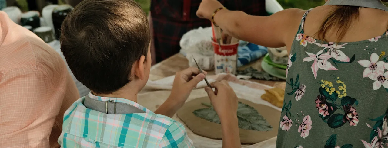 Two people engaged in a creative activity, pressing leaves into clay and using tools. A cup with the word Happy is on the table.