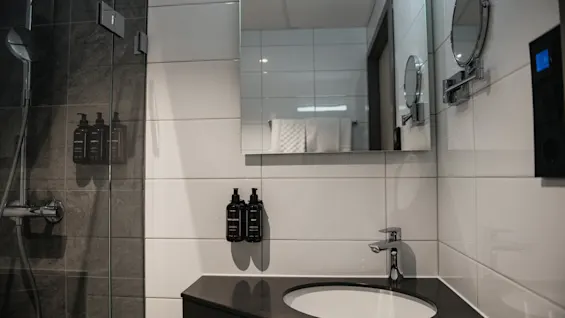 Et elegant bad med en glassdusj, en servant med skap og et speil, klart for personlig pleie.