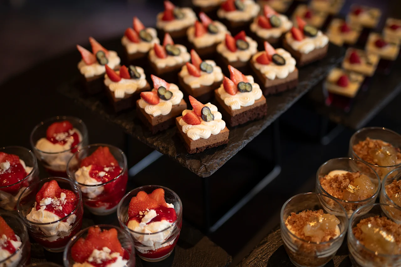 Et dejligt udvalg af forskellige desserter, herunder små kager toppet med bær og cremede parfaits i glas.