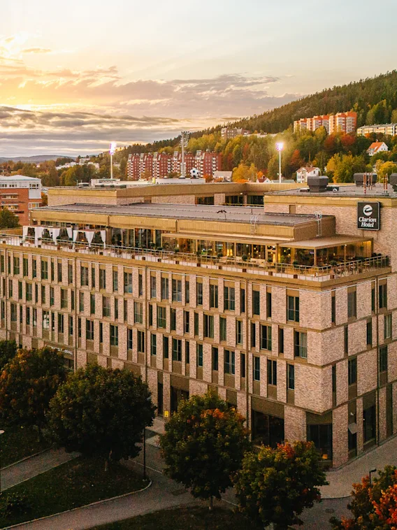 En imponerande hotellbyggnad med en livlig takterrass, badad i solnedgångens varma sken, med en naturskön sluttning bakom.