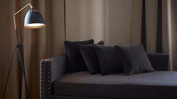 A floor lamp illuminates a sofa with cushions against a backdrop of draped curtains.
