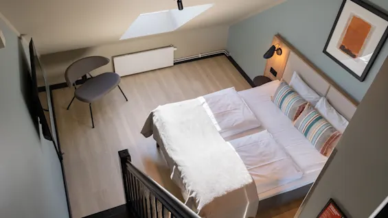 Ett mysigt, modernt hotellrum med en bekväm säng, en stilren stol och ett sluttande tak med takfönster.