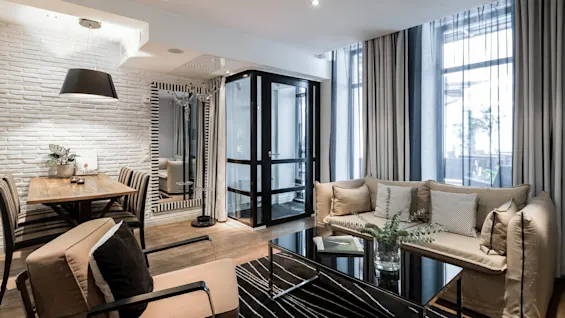 Koselig stue og spisestue med beige sofa, stripete gardiner og trebord under en svart pendellampe. En glassdør fører ut. Gulvet er av tre, og innredningen er moderne.