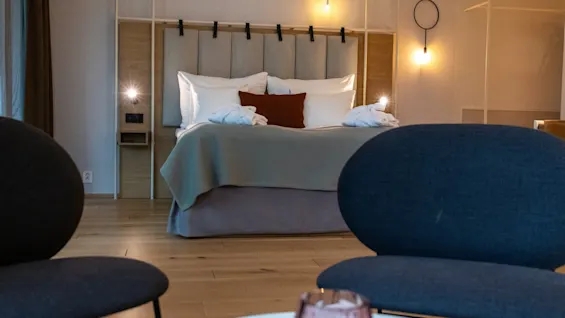 Et moderne hotellrom med en oppredd dobbeltseng, koselig belysning og to mørke lenestoler i forgrunnen.