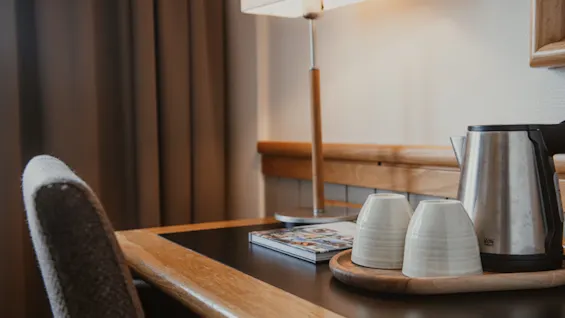 A cozy desk area with a lamp, a book, and a tea set with a kettle and two cups, ready for a relaxing break.