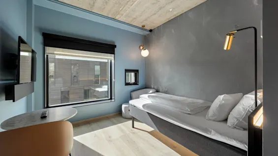 Et moderne og koselig hotellrom med en komfortabel seng, et vindu som gir naturlig lys og et lite sitteområde.