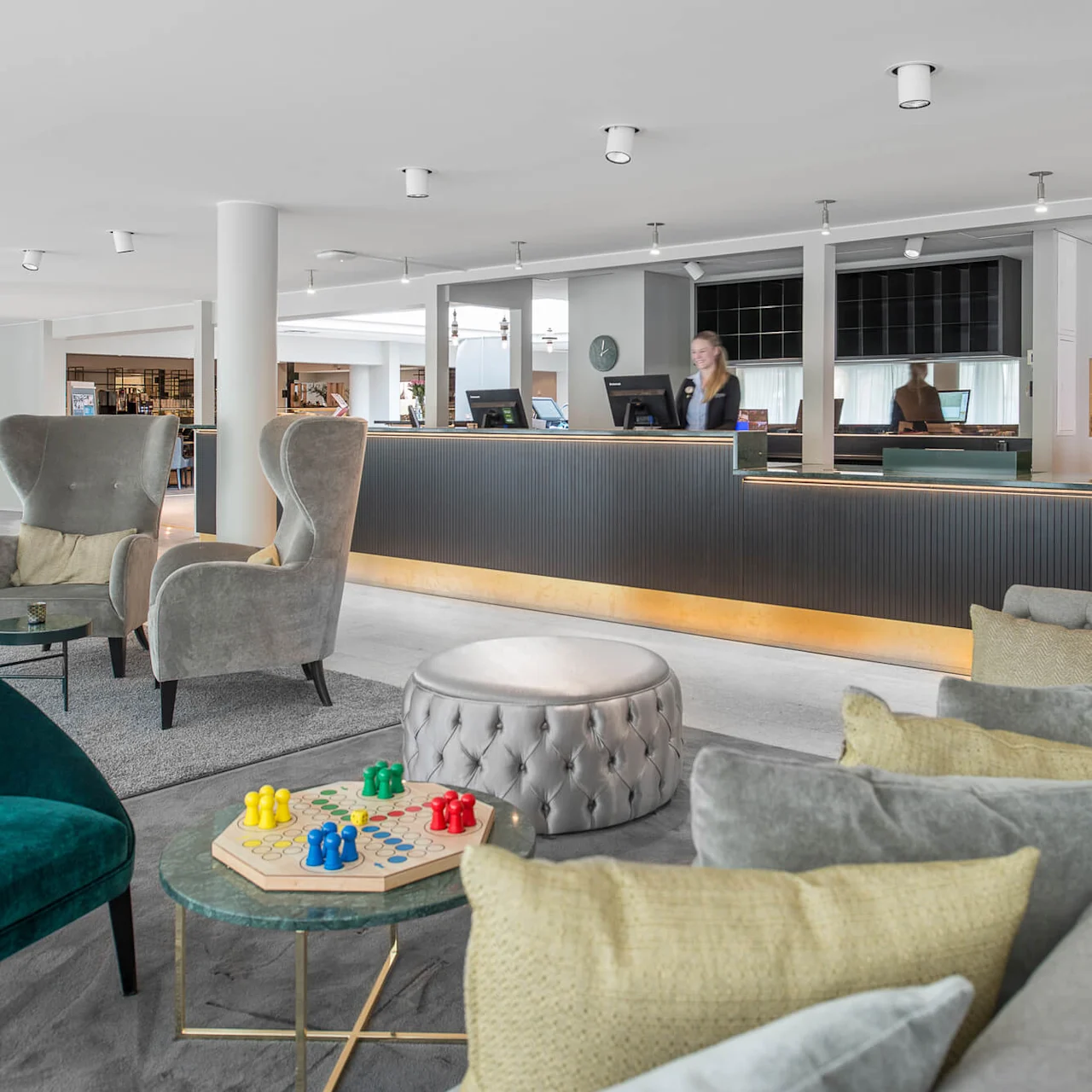 En modern hotellobby med mjuka fåtöljer och ett litet bord med ett brädspel. En receptionist står vid den eleganta, svarta disken. Ljust, luftigt inredning förstärker den rymliga atmosfären.