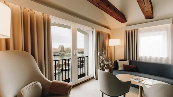 Mysig hotellsvit med sofa, fåtöljer och stora fönster med vacker utsikt över vattnet.