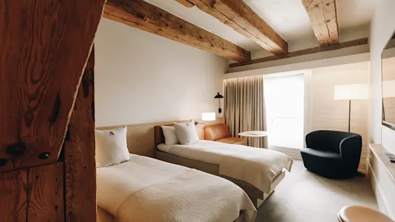 Ett mysigt hotellrum med två enkelsängar, synliga träbjälkar i taket och en bekväm sittgrupp vid fönstret.