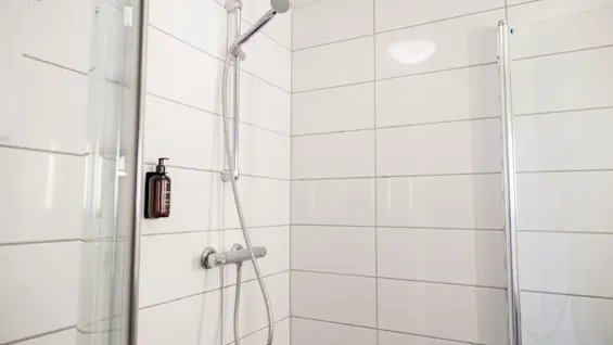 Et moderne brusebad med hvide flisevægge, et krom brusehoved og en sæbedispenser, klar til en forfriskende vask.